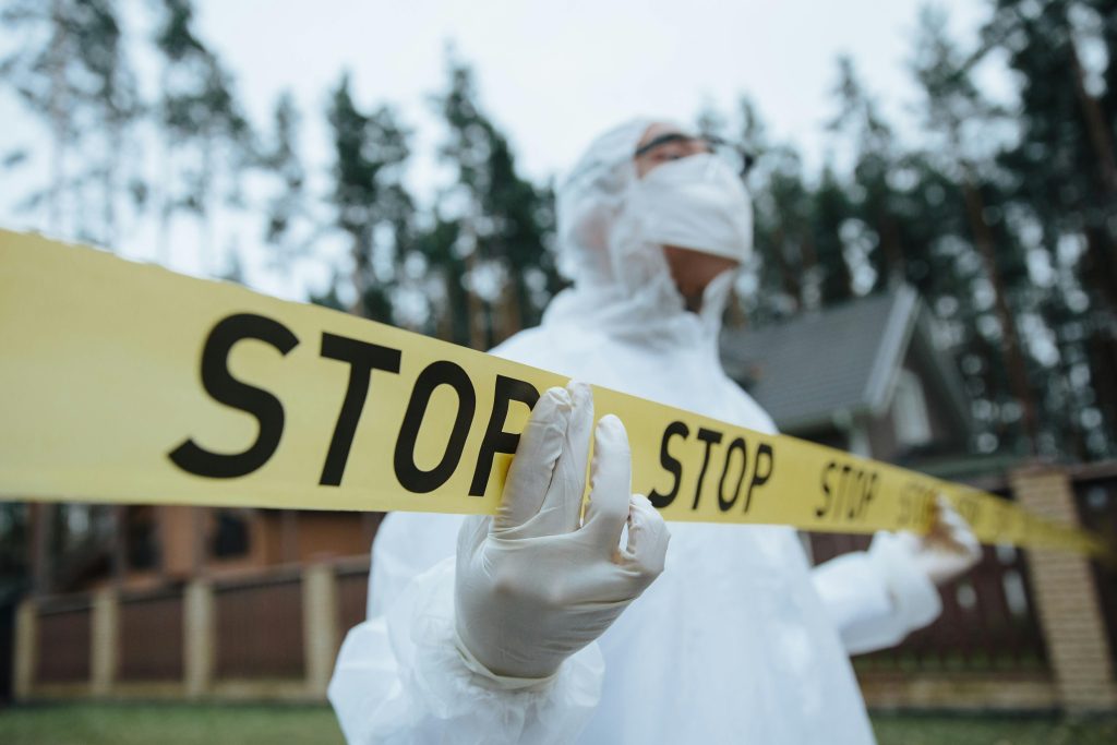 pexels-photo-10481262-10481262 Investigator in protective gear securing crime scene with stop tape outdoors.